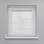 Closed window blinds in white frame casting shadows on grey wall. Minimalistic design with soft natural light filtering through slats.